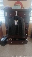 Men's black leather steampunk jacket hanging on a hanger in front of a dresser.