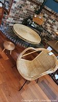 Photo of all three items - wicker chair, small stool, and round table together on wooden floor with brick wall background.