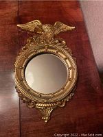 Full front view of the vintage gold leaf Federal eagle mirror showing detailed eagle perched on the round mirror frame on a wood surface.
