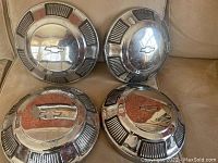 Four Chevrolet dogdish style hubcaps arranged on a beige surface showing size and wear.