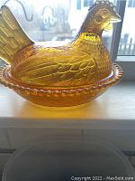 Side view of amber glass candy dish showing detailed molded hen atop nest base with beaded rim.