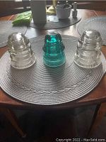 Three glass insulators on a table in natural light showing two clear 'Dominion' insulators and one green 'New York and Brookfield' insulator.