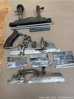 Photo showing the Stanley #45 combination plane body, wooden handle, 14 cutters laid out, rods, and fence accessory on a flat surface.