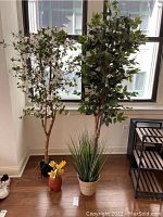 Wide view of two tall artificial trees, one with white flowers and one green, with the two smaller potted artificial plants in front.