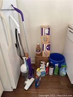 Wide shot of all items including mop, vacuum, cleaning liquids, and bucket.