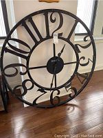 Front view of the large round metal wall clock with open number design and distressed black finish.