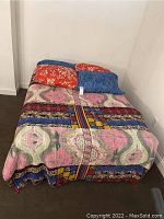 Full view of full size bed with colorful bedding and pillows against white walls in room