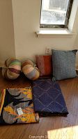 Full set of handmade textile items including two throw quilts and four throw pillows arranged on floor near window.