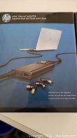 Photo of HP 65W Slim AC Adapter packaging showing adapter, cable and multiple connector tips.