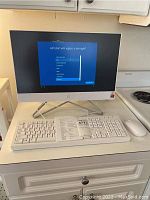 Full view of HP all-in-one desktop powered on showing Windows setup screen, with keyboard and mouse on countertop