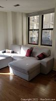 Full view of light gray upholstered Ikea sofa with chaise placed by windows, showing overall condition and accessory pillows.