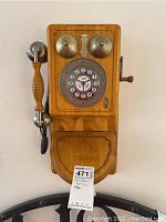 Front view of vintage style wall mounted telephone with wooden case, rotary dial, metal bells, and handset on side.