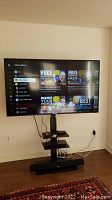 65" Sceptre TV powered on atop the media stand showing overall setup including shelves and sound bar