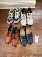Four pairs of men's size 10 shoes, two athletic sneakers and two dress shoes, arranged on wooden floor.