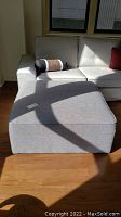 Grey upholstered ottoman angled with sectional couch in background, showing size and fabric texture