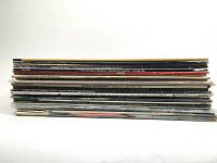 Side view of 18 vinyl LP records stacked horizontally showing variation in cover colors and spines with artist names and album titles.