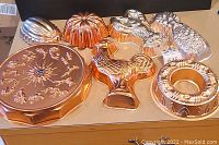 Seven copper and metal kitchen molds including rooster, sun with astrological signs, wreath, pineapple, lobster, and two pudding molds.