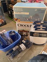 Photo showing lots of kitchen items including boxed 7 quart Crock-Pot Classic slow cooker, Anchor Hocking 22 piece glass bake set, blue utensil holder, blue utensils, blue dish tub, and cutting boards.