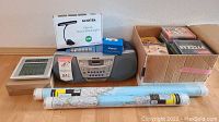 Full lot overview showing digital clock, Sony radio cassette player, KOOTEK clip-on stand light box, music CDs in cardboard box, and two rolled maps.
