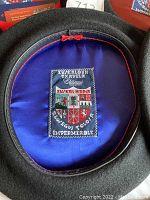 View of inside lining of black beret showing blue satin lining and embroidered Basque coat of arms label 'EUSKALDUN TXAPELA ELOSEGUI TOLOGI IMPERMÉABLE'