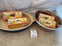 Blue Le Creuset oval casserole dish, multiple pasta maker attachments in boxes on top, large perforated stainless steel colander