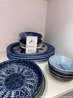 Overview of blue and white pottery and ceramic serving items stacked on shelf, including plates, bowls, and platters.
