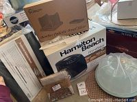 Photo showing Hamilton Beach HomeBaker bread maker box, Purenjoy Bamboo Foldable Bread Slicer box, linen bread bags packaging, cooling tray, and other items in original packaging.