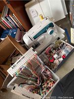 Brother XL-2600i sewing machine with white carrying case and assorted colorful embroidery floss attached to a holder with thread labels.