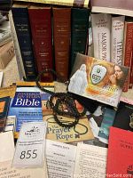 Four large hardcover volumes of The Liturgy of the Hours with large type editions in dark blue, red, brown, and green covers, stacked vertically; electronic rosary device box and black bead rosary in front.