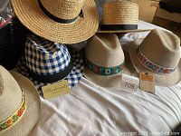 Collection of six men's hats - five Panama hats by Sterkowski including three in sand-colored burlap with floral bands and one in blue and white check with black band, plus two straw boater hats with black grosgrain ribbon trim laid out on white surface.