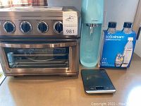 All included items shown together on countertop: oven, SodaStream machine, bottles box, digital scale