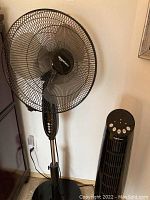 Front view of the black Amazon Basics oscillating floor fan beside the digital tower fan.