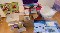 Overview of the lot with tackle boxes, boxes of wire, sewing supplies, paper and labels on floor