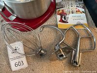 Three metal attachments and quilted cover in front of red mixer base