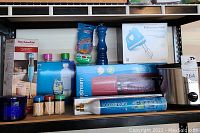 Photo showing various boxed and unpacked kitchen equipment including KitchenAid hand mixer and blender, SodaStream with cylinders and bottles, salt shaker, pepper grinder, kosher scrubbers, and toothpick dispensers.