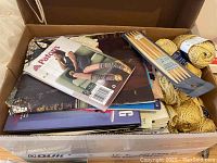 Photo of cardboard box containing knitting pattern booklets, knitting needles, and yellow yarn skeins.