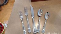 Two dinner forks, one table knife, one soup spoon and one teaspoon from Lenox flatware set displayed on countertop