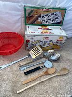 Photo showing the boxed Marcato Multipast pasta maker set with attachments and Raviolamp tortellini mold along with various kitchen utensils and red colander.