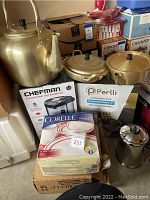 Photo showing golden toned Korean kettle, two saucepans with lids, Perlli cookware box, Chefman electric hot water pot box, Corelle Livingware dinnerware box, and Farberware stainless steel coffee maker.