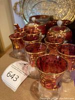 Full view of 12 Persian style tea/coffee glasses with red and gold grape motif and portraits, with sugar bowl and teapot behind and tray at the back.