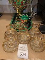 Five clear glass tea cups seated on etched saucers in front of green floral samovar and tray