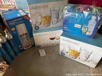Photo showing boxed rose gold SodaStream Fizzi machine, Dailyware glassware sets, and CO2 cylinders together.