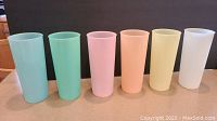 Six tall pastel cups in colors green, blue, pink, orange, yellow, and white aligned on a surface.