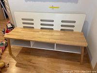 Front view of wooden bench showing seat surface, backrest with horizontal cutouts, and open storage compartments underneath.