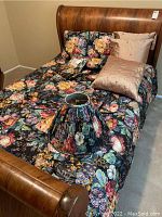 Full size wooden bed with floral comforter, pillows, and lampshade placed on the bed