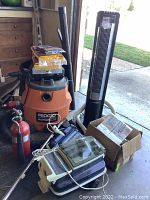 Overview of lot showing Ridgid Blower Vac, Eureka vacuum, Sylvania tower fan, two fire extinguishers and cardboard box with accessories.