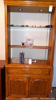 Front view of wooden bookcase with glass shelf containing glasses, a picture frame, and other small items. Shows overall structure and detail.