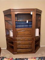 Front view of the wooden corner bookcase with shelves, drawers, and drop-front cabinet showing its detailed woodwork and brass handles.