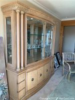 Full front view of large blonde wood china cabinet with glass doors and display shelves, showing overall structure and detailing.