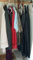 Side view of assorted jackets and shirts hung on rack including the cream jacket, dark jackets, plaid and patterned shirts